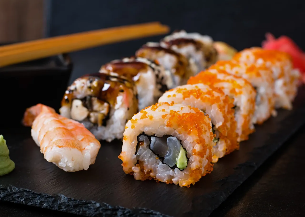 R&oacute;żnorodne rolki sushi, w tym te z ikrą tobiko i polane sosem, kuszą wizualnie. Zastanawiasz się, ile sushi na osobę to idealna porcja?