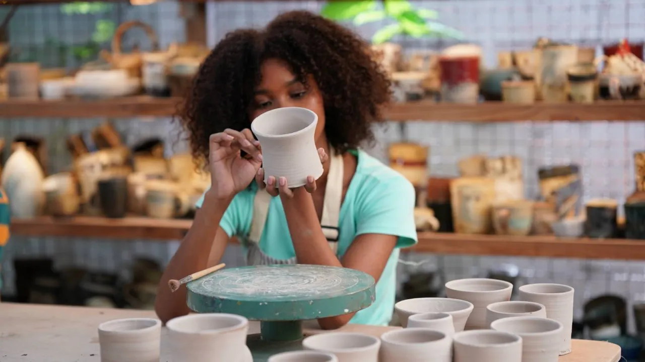 Młoda artystka tworzy ceramikę, zastanawiając się, co to za piękny proces. Na stole stoją gotowe naczynia.