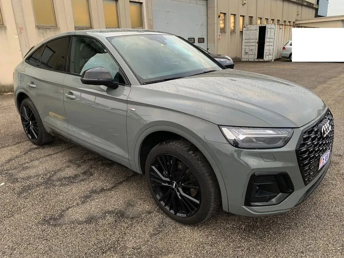 Szary Audi Q5 Sportback na placu, gdzie handlarze kupują auta w Niemczech. Czarne felgi i sportowy wygląd.