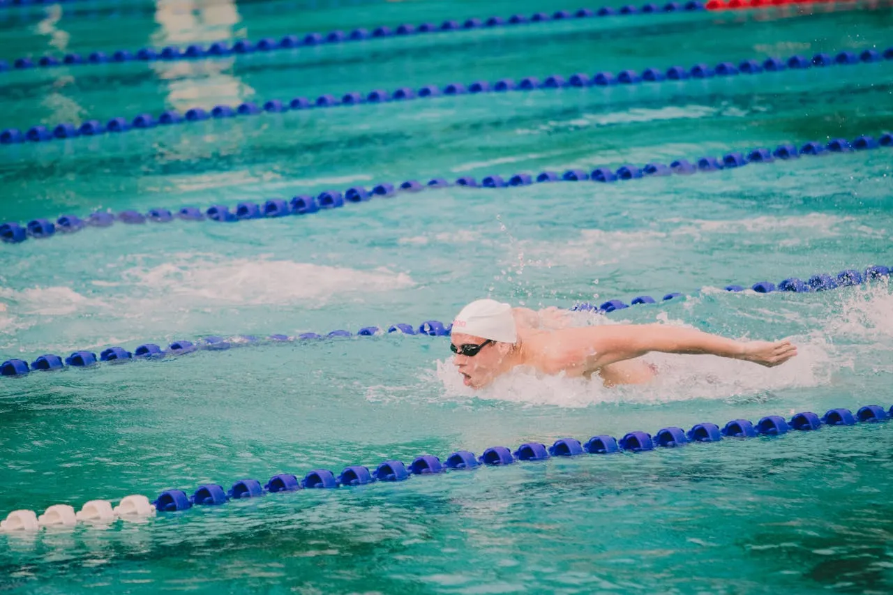Pływak w czepku i okularach demonstruje, jak się pływa żabką, pokonując wodę w basenie.