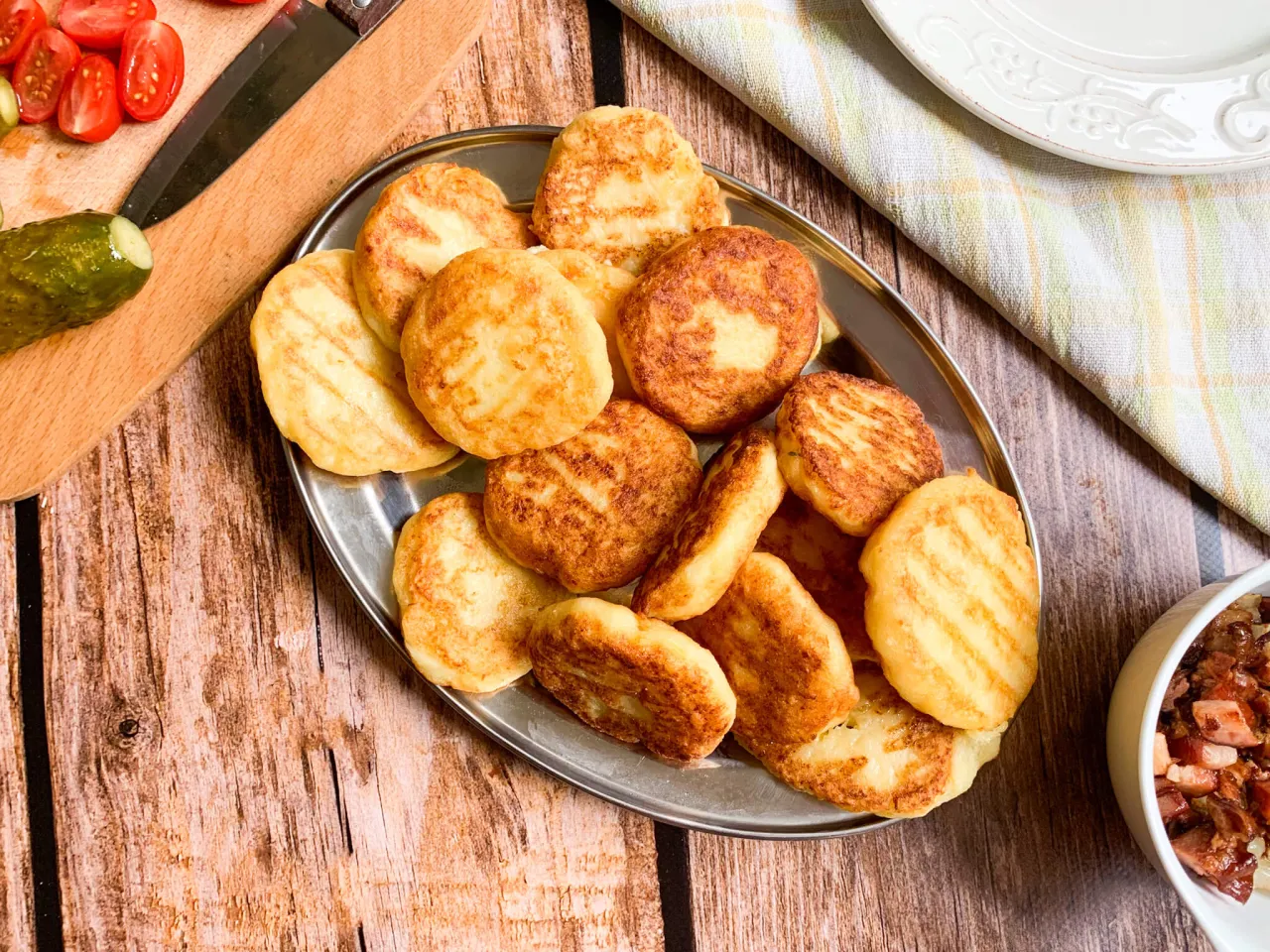 Placki ziemniaczane na talerzu, idealne do restauracji bac&oacute;wka menu. Obok pomidorki, og&oacute;rek i miseczka z dodatkami.