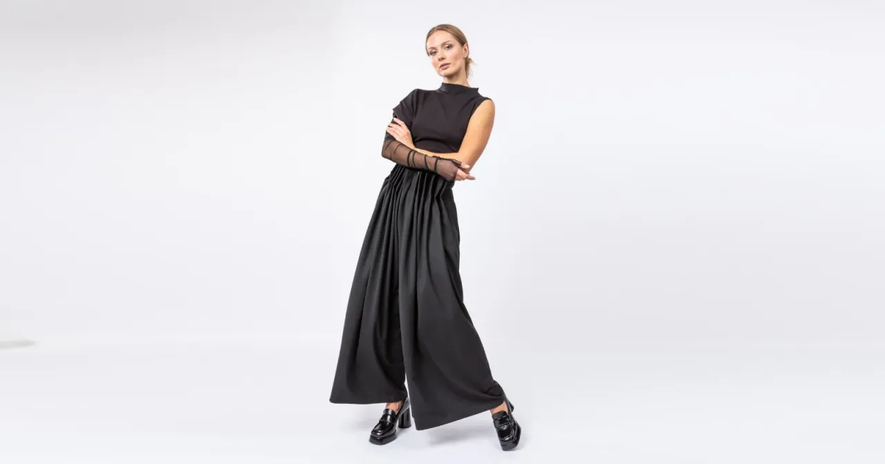 Elegancka kobieta w czerni, idealna stylizacja w czym do teatru. Szerokie spodnie i bluzka z siateczkowymi rękawami.