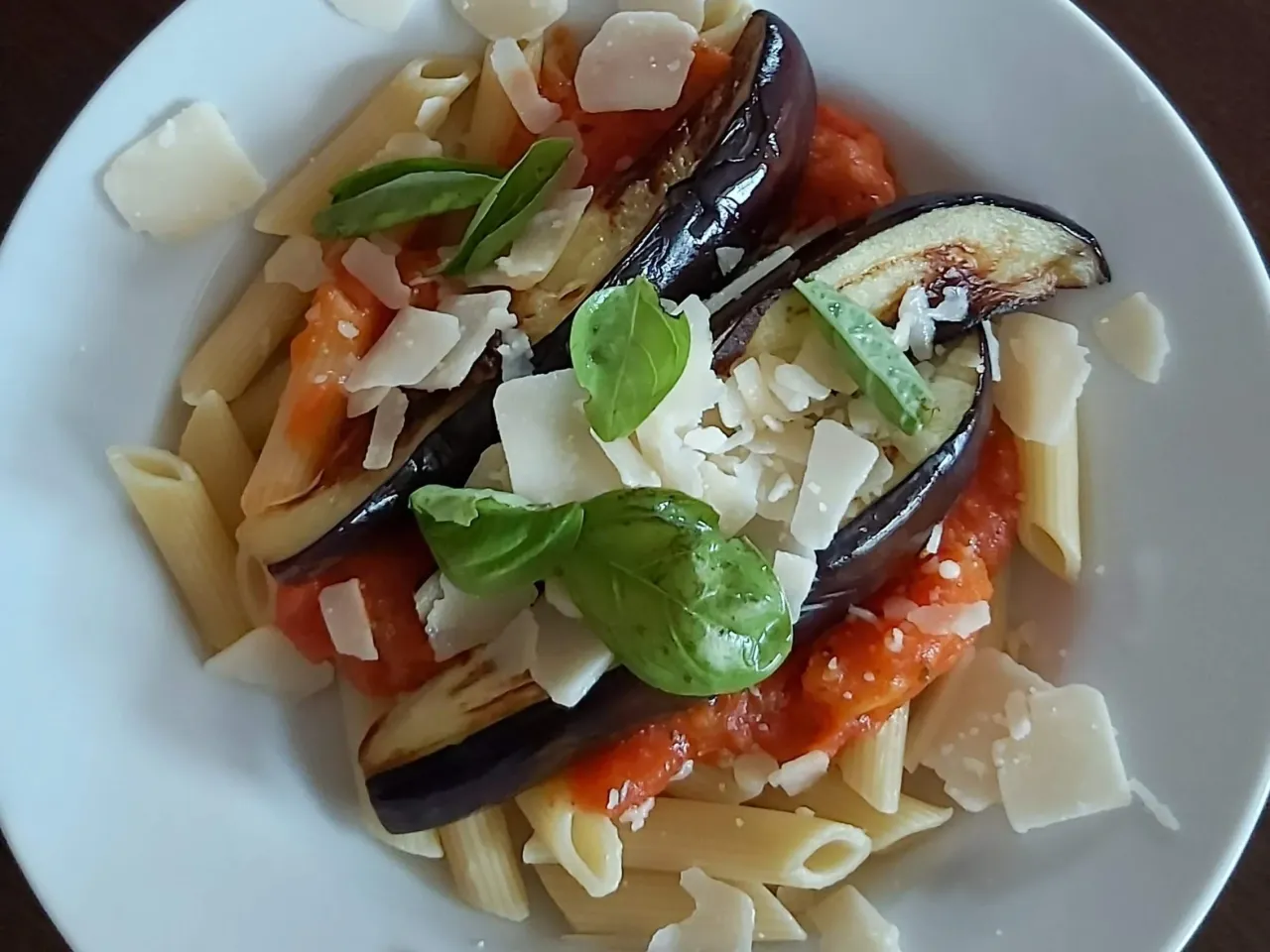 Penne z bakłażanem i pomidorami, posypane parmezanem i bazylią. Idealne Pasta alla Norma przepis.