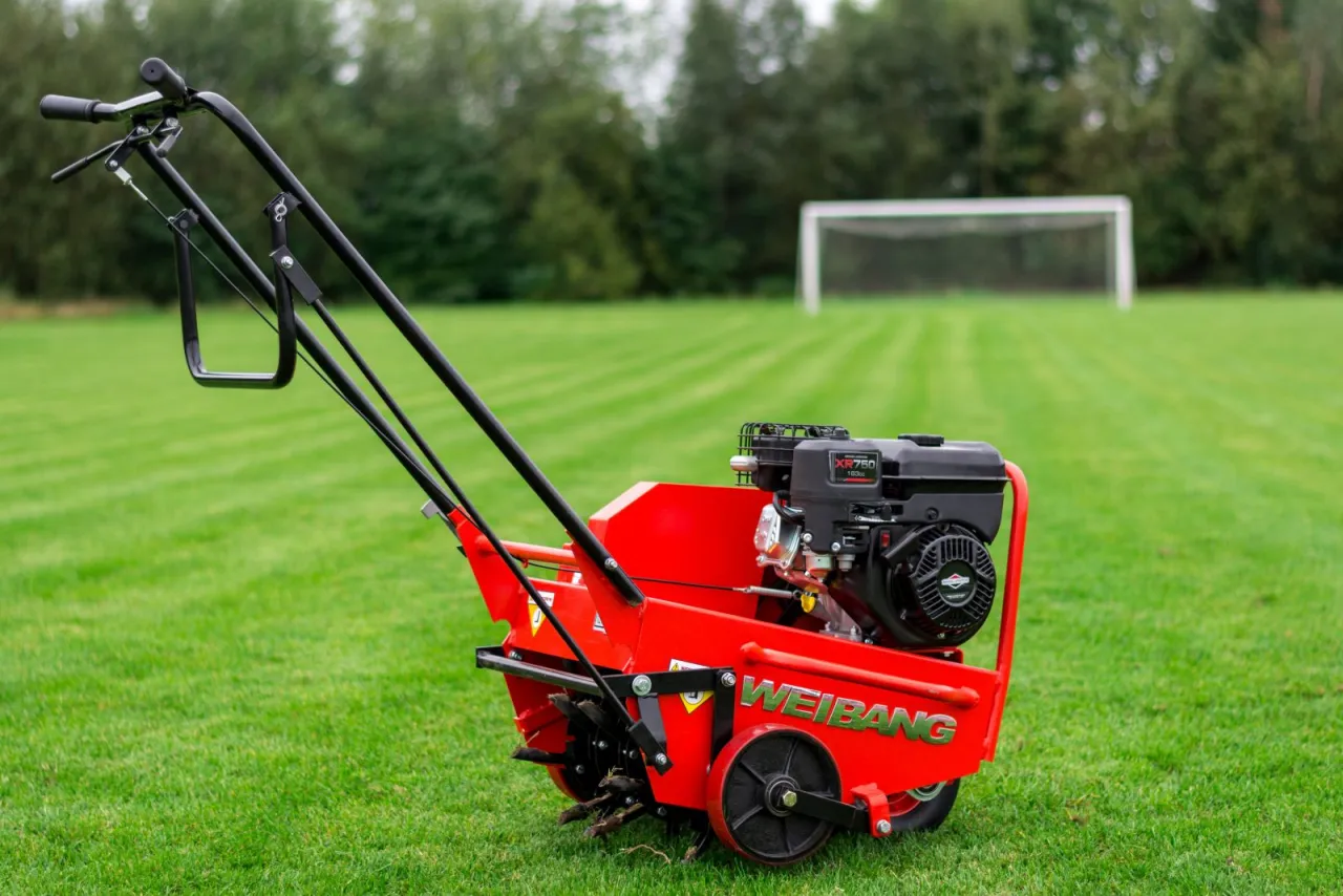 Czerwony wertykulator Weidemann na zielonej trawie. Do czego służy wertykulator? Do napowietrzania i usuwania mchu z trawnika, by lepiej rósł.