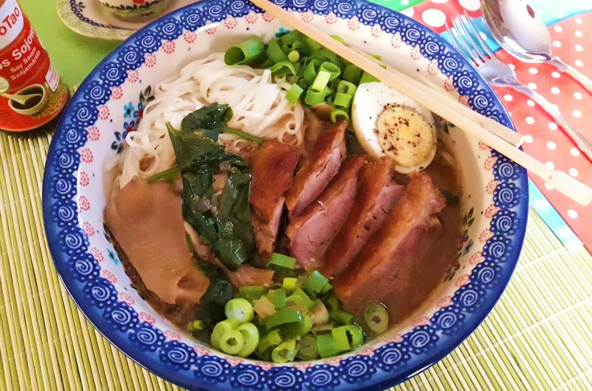 Aromatyczny ramen z kaczki z makaronem, jajkiem, zieloną cebulką i grzybami w ozdobnej misce.