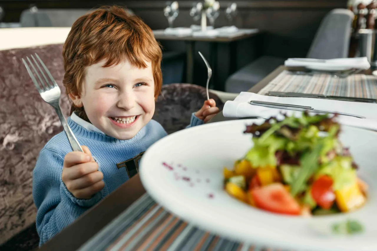 Uśmiechnięty rudowłosy chłopiec z widelcem w ręku, gotowy do jedzenia sałatki. Może to być inspiracja, co na obiad dla niejadka.