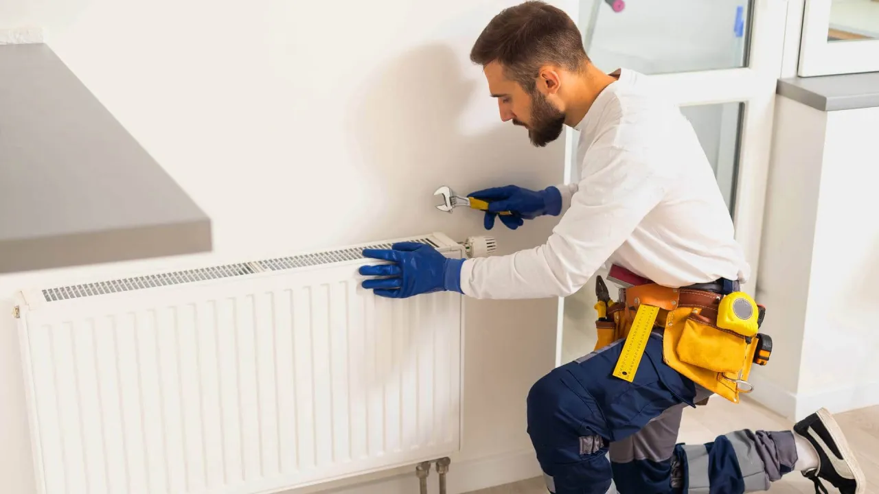 Fachowiec w niebieskich rękawiczkach odpowietrza grzejnik, używając klucza. To kluczowy krok, by dowiedzieć się, jak odpowietrzyć piec co.