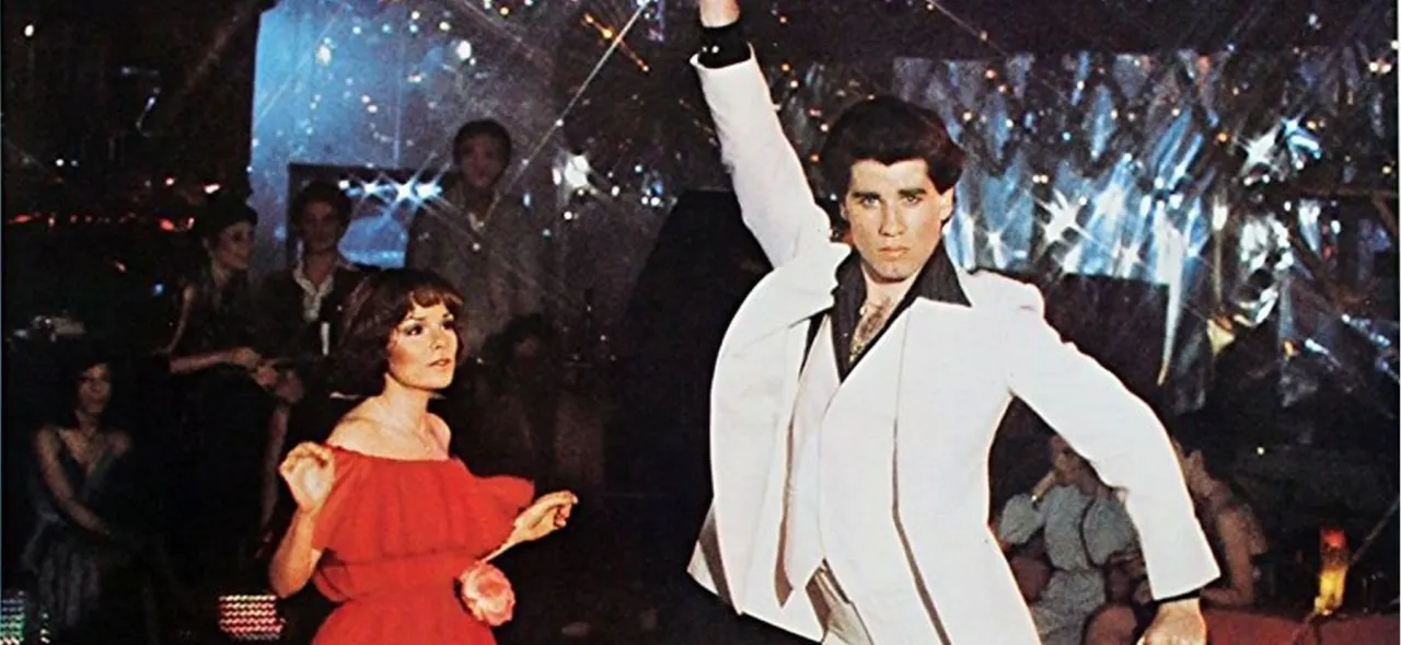 John Travolta w białym garniturze tańczy na parkiecie, a obok niego kobieta w czerwonej sukience. To kwintesencja gorączki sobotniej nocy.