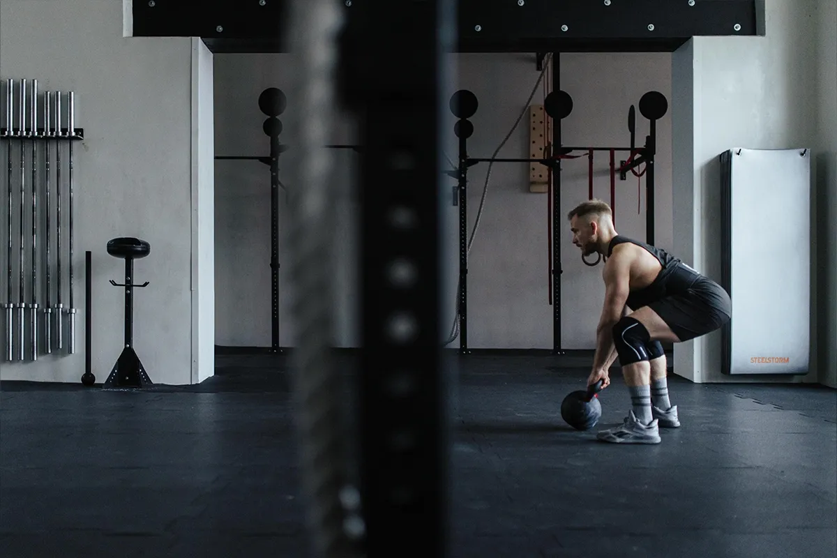 Mężczyzna w siłowni przygotowuje się do podnoszenia kettlebell. Zastanawia się, jakie odżywki na crossfit będą najlepsze.