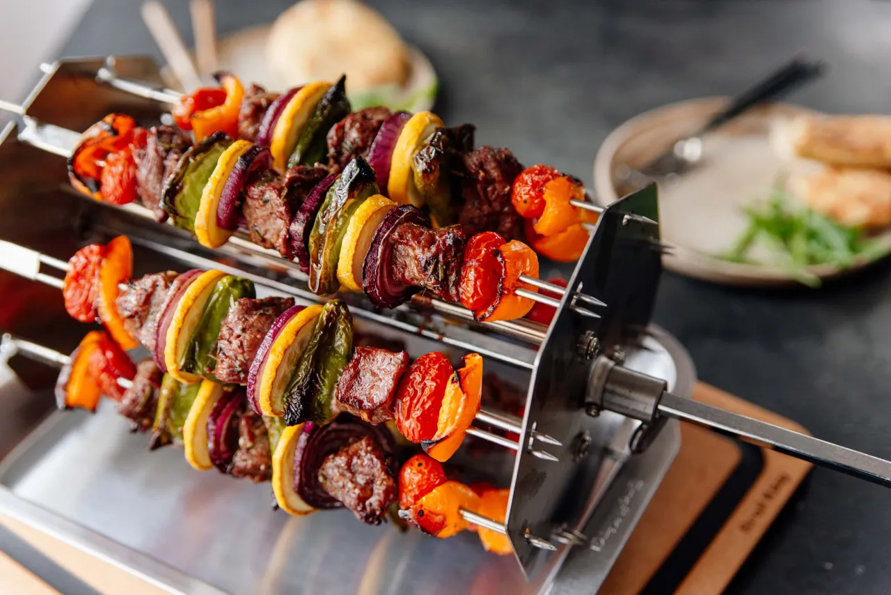 Na obrotowym rożnie piecze się kilka szaszłyk&oacute;w z mięsem, papryką, cebulą i cytryną.