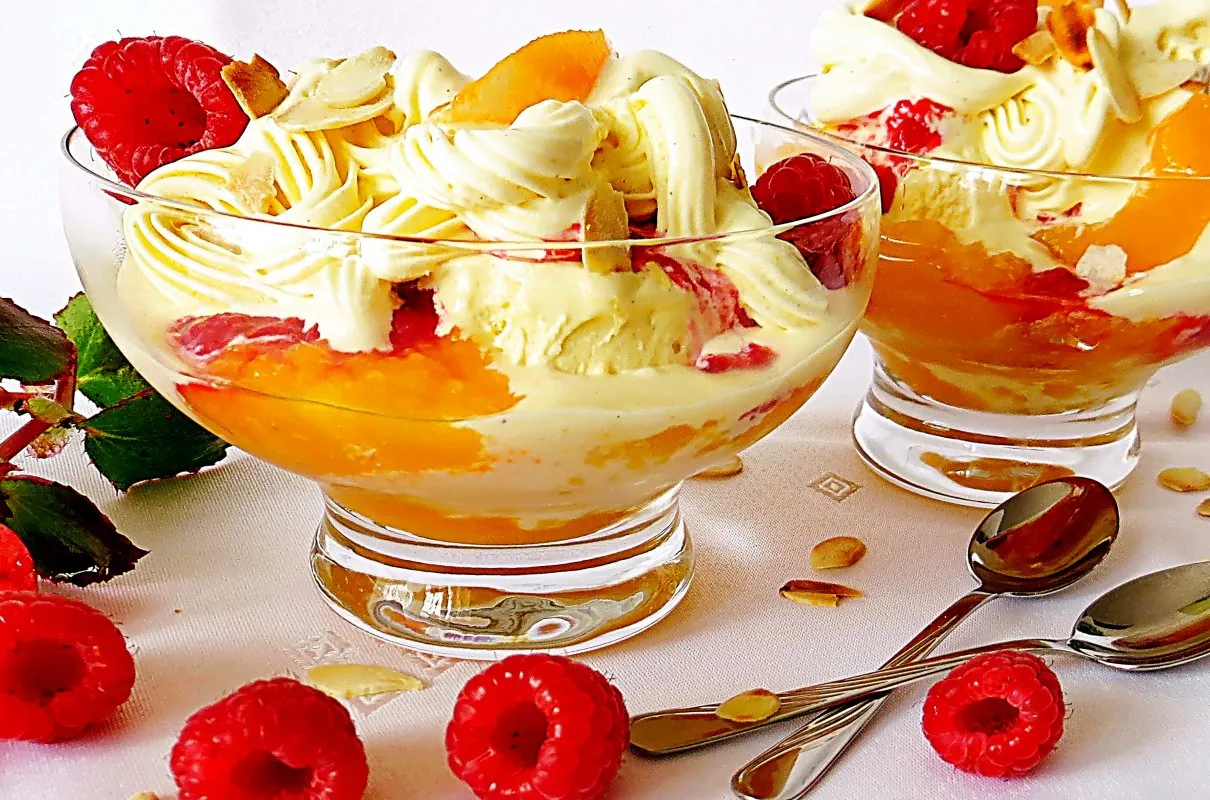 Pyszny deser Melba przepis: lody waniliowe z brzoskwiniami, malinami i bitą śmietaną, posypane płatkami migdałów.