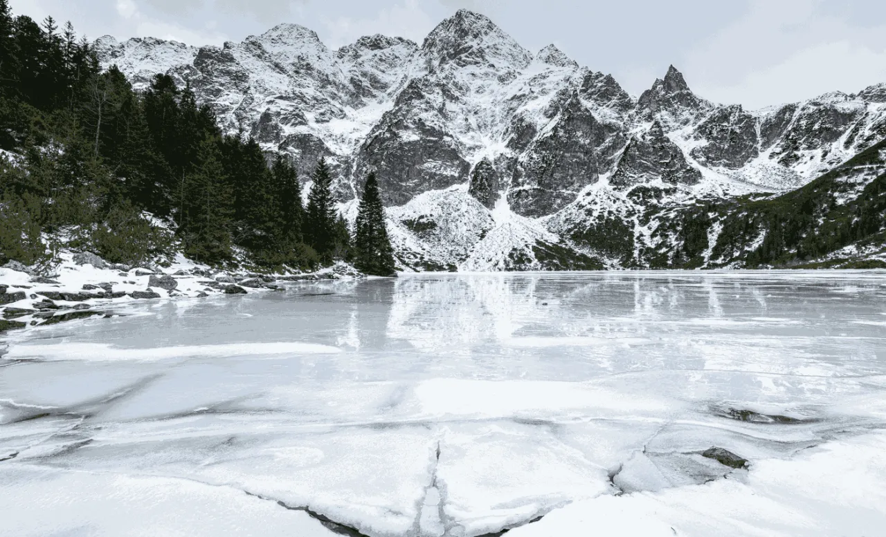 Mroźne jezioro i ośnieżone szczyty Tatr. Bukowina Tatrzańska oferuje zimowe atrakcje, jak wędrówki po górach i podziwianie krajobrazów.