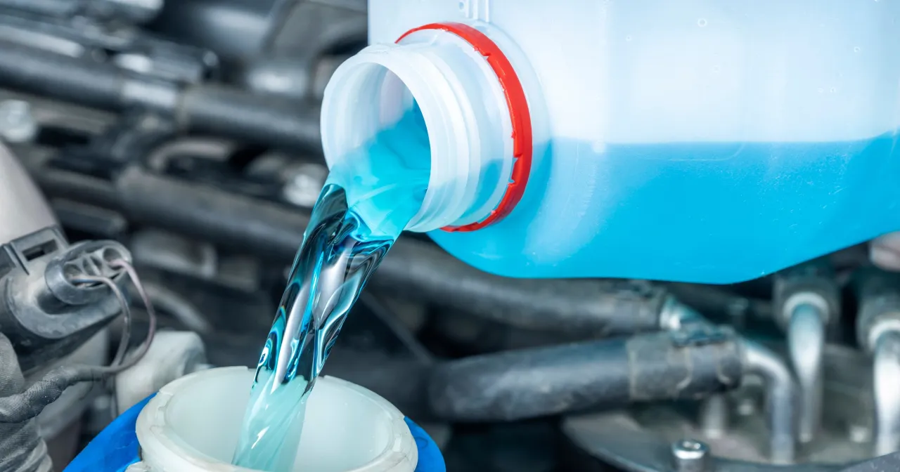 Niebieski płyn do spryskiwaczy leje się z butelki do zbiorniczka. Uzupełnij go, by uniknąć mandatu za brak płynu do spryskiwaczy.