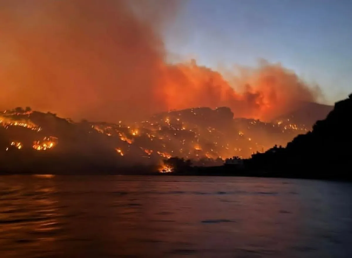 Pożar na zboczu góry na Krecie. Płomienie i dym unoszą się nad domami. Czy jest bezpiecznie?