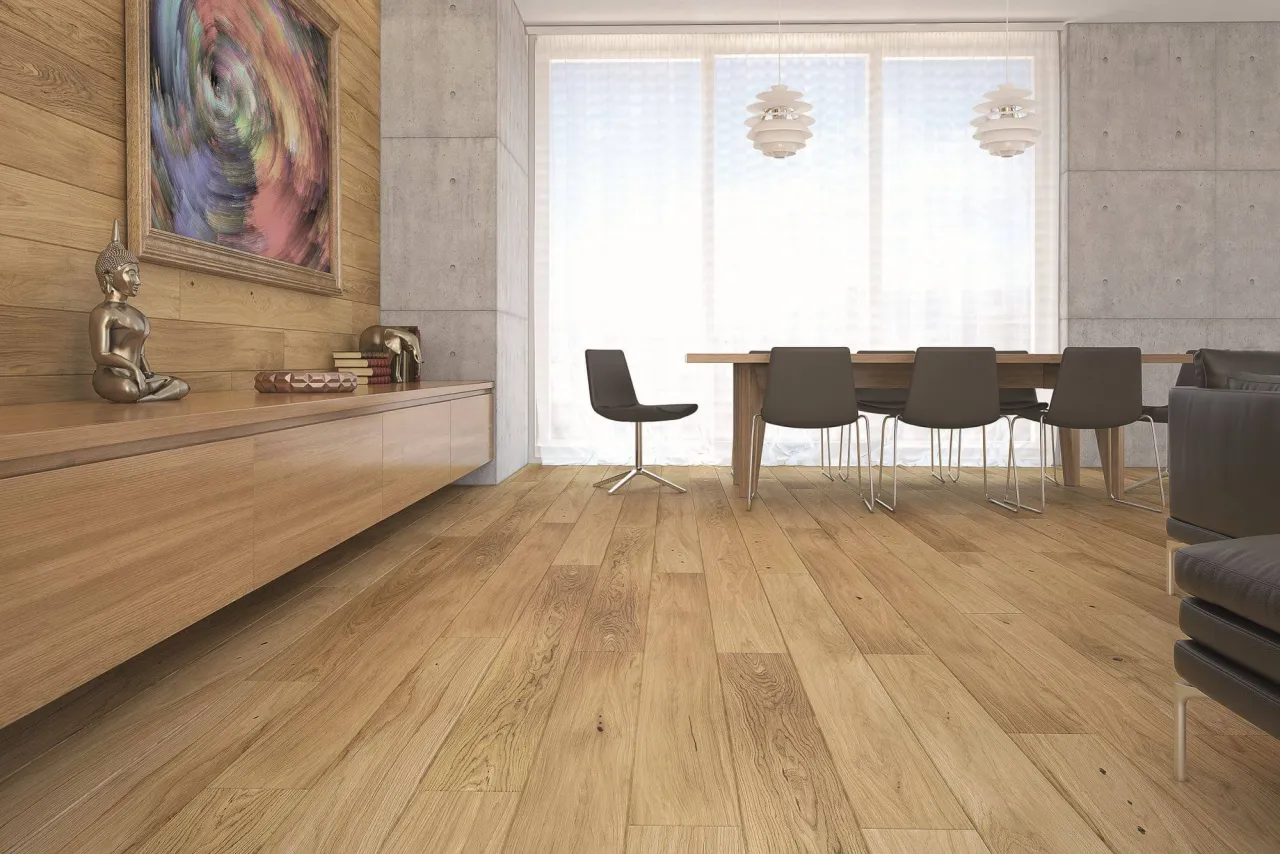 Drewniana podłoga w salonie z jadalnią. Panele ułożone wzdłuż, tworząc spójną całość. W tle betonowa ściana i okno.