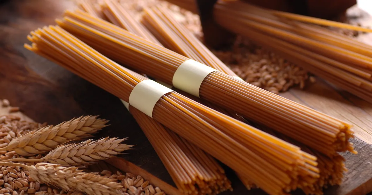 Makaron pełnoziarnisty vs zwykły. Zboża i kłosy pszenicy obok pęczków makaronu spaghetti.