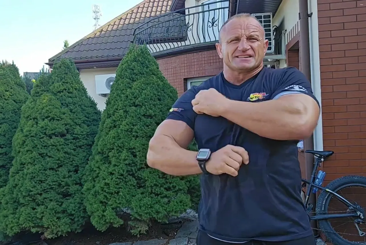 Mariusz Pudzianowski napina bicepsy przed swoim domem. W tle widać zadbane tuje i fragment domu, gdzie mieszka Pudzian.