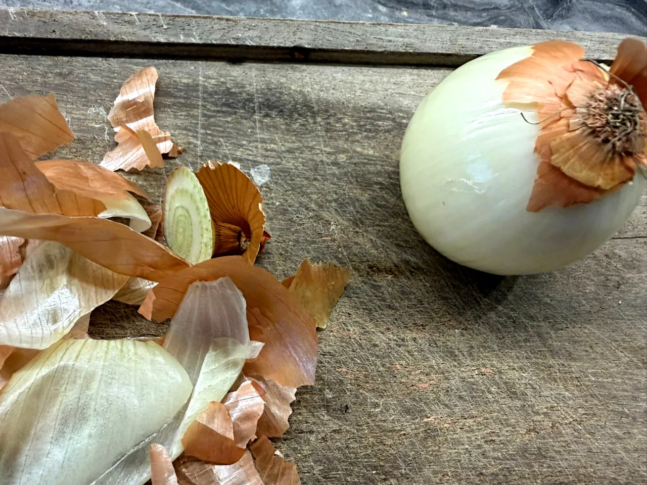Obierki cebuli i cała cebula na desce. Czy można mrozić cebulę? Tak, można ją mrozić, ale najlepiej pokrojoną.