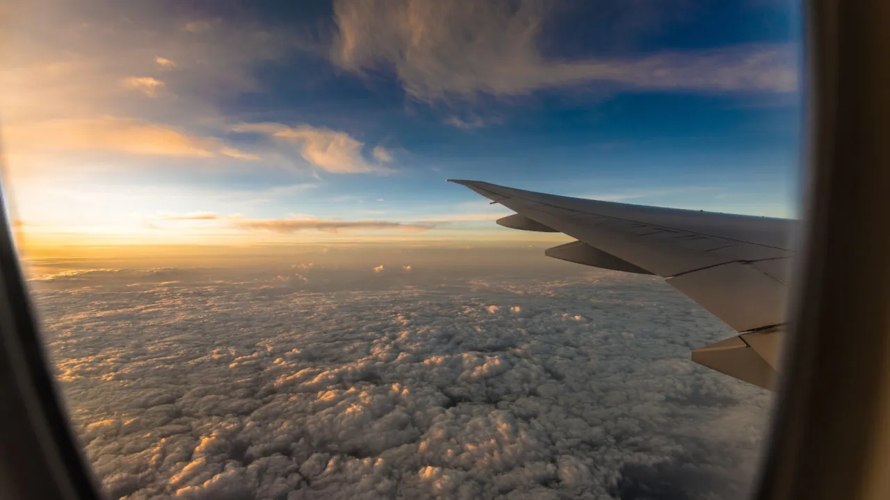 Widok z okna samolotu na morze chmur o zachodzie słońca. Skrzydło samolotu, jakby w podr&oacute;ży z Ryanair od kiedy loty.