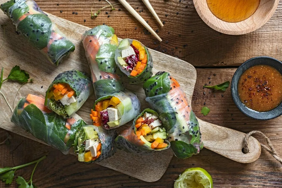Kolorowe rolls z papieru ryżowego z warzywami i tofu, podane na desce z sosem.