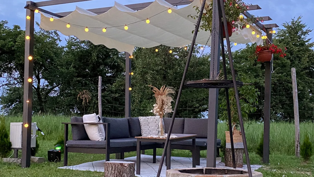 Jak urzadzic pawilon ogrodowy: przytulna strefa relaksu z sofą, stolikiem, girlandą świateł i paleniskiem.