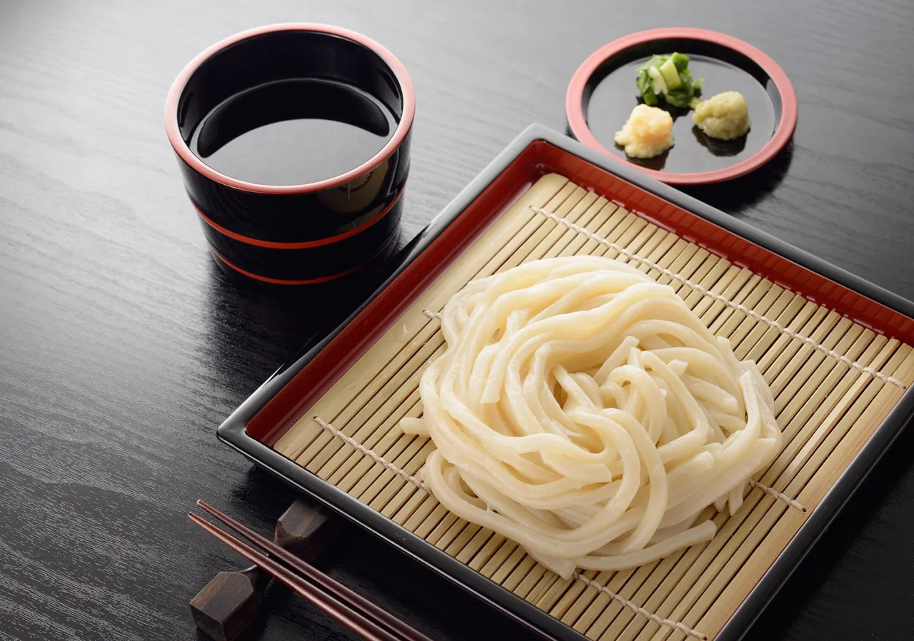 Jak gotować makaron udon: świeży, gruby makaron na bambusowej macie, miseczka z sosem i dodatkami.