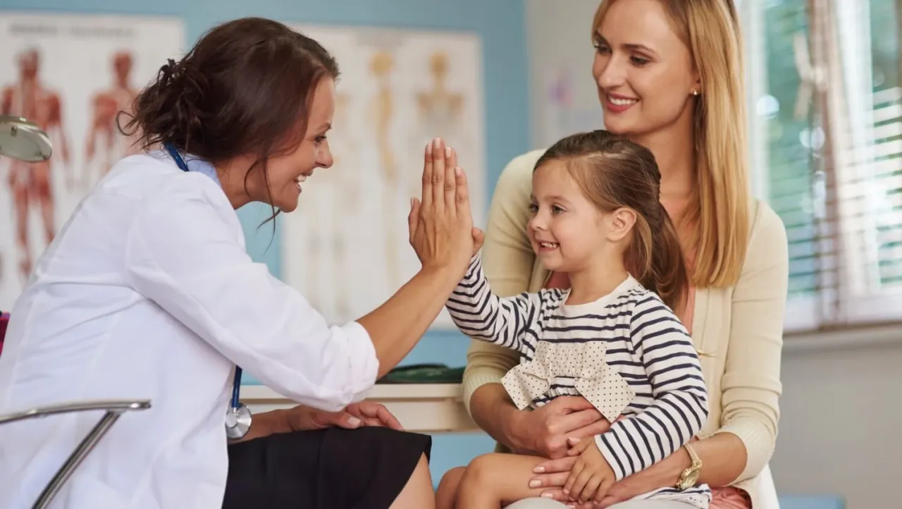Lekarka daje piątkę małej pacjentce, która jest z mamą. To miłe zakończenie wizyty, pokazujące, co to jest bilans u lekarza – zdrowie i radość.