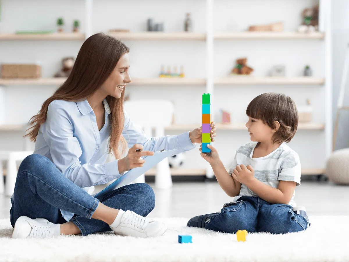 Terapeuta pomaga dziecku układać wieżę z klock&oacute;w. To jak zagadka z odpowiedzią, gdzie każdy klocek to krok do rozwiązania.