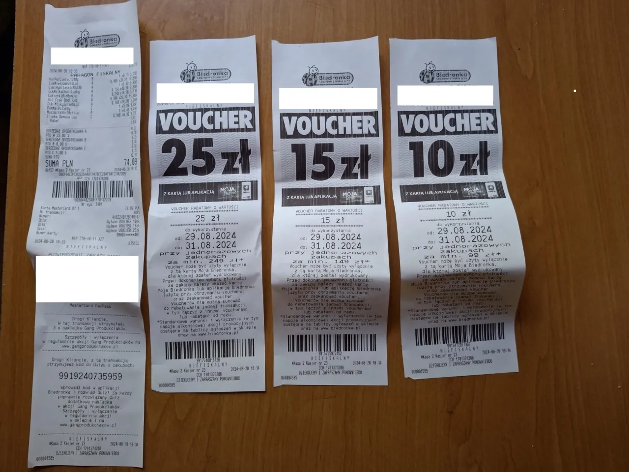 Na zdjęciu widać paragon z Biedronki oraz trzy kupony rabatowe. Paragon pokazuje, jak wygląda faktura z Biedronki, z listą zakup&oacute;w i cenami. Kupony mają wartości 25 zł, 15 zł i 10 zł.