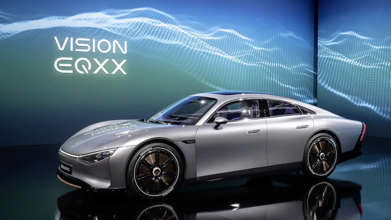 Srebrny, futurystyczny samoch&oacute;d elektryczny Vision EQXX, kt&oacute;ry obiecuje zasięg 1000 km, prezentowany na tle niebieskiej, falującej grafiki.