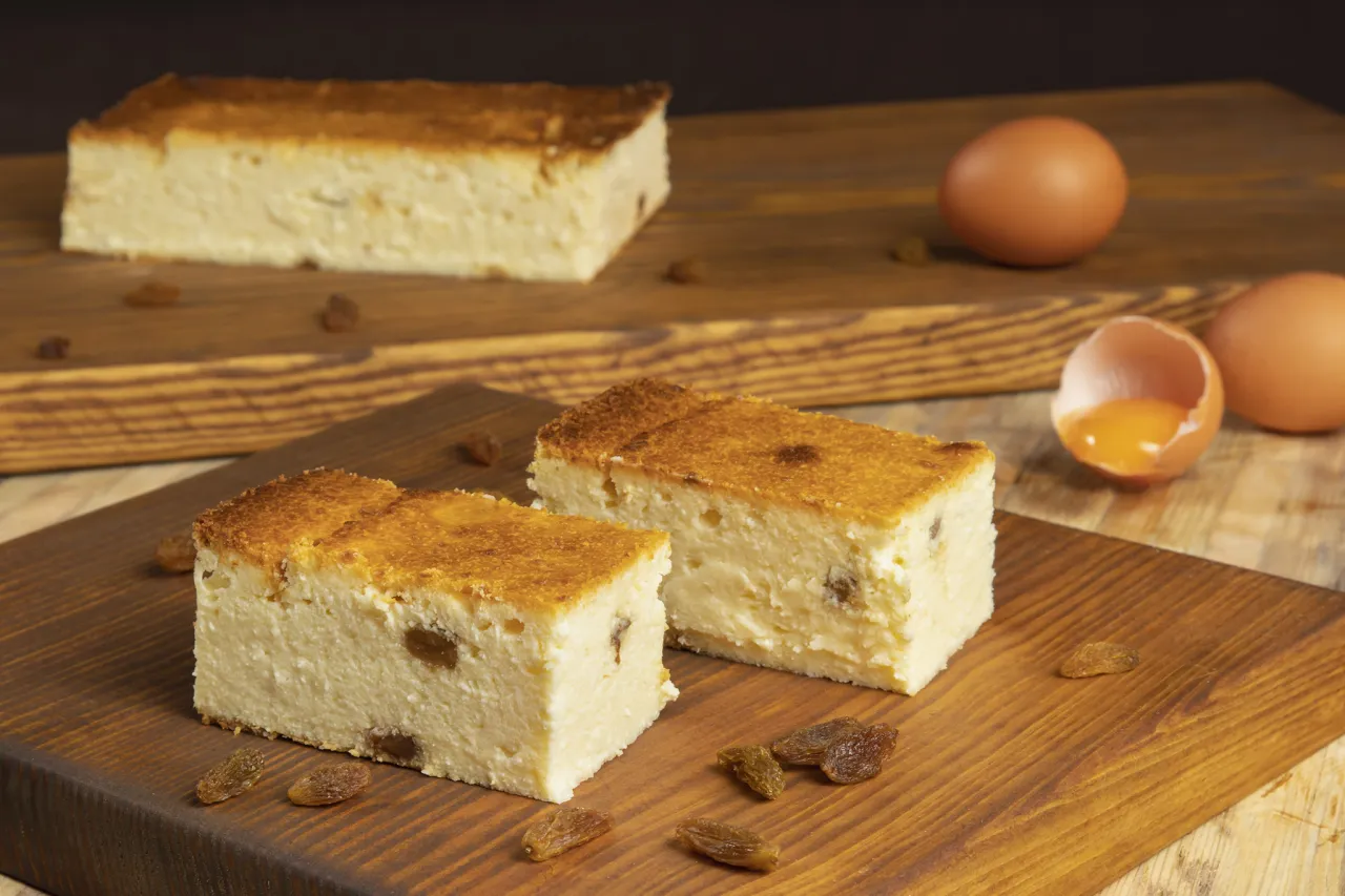 Dwa kawałki sernika z rodzynkami na drewnianej desce. Obok jajka i skorupka z żółtkiem. Zastanawiasz się, ile waży sernik?