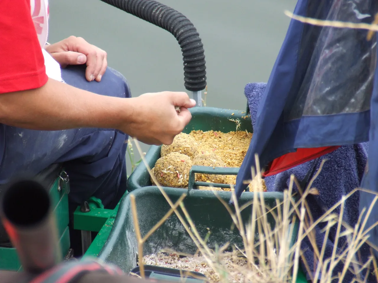 Wędkarz przygotowuje zanęty Marcel na zawody. Widać rękę z robakami i pojemnik z mieszanką.