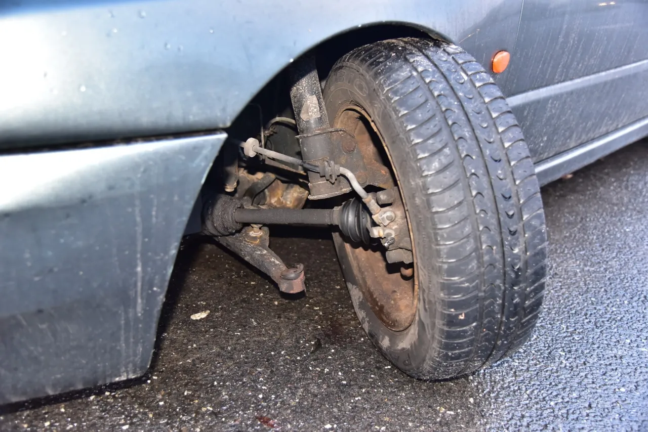 Widok na zawieszenie samochodu, koło i elementy układu kierowniczego. Pokazuje, jak sprawdzić sworzeń wahacza.