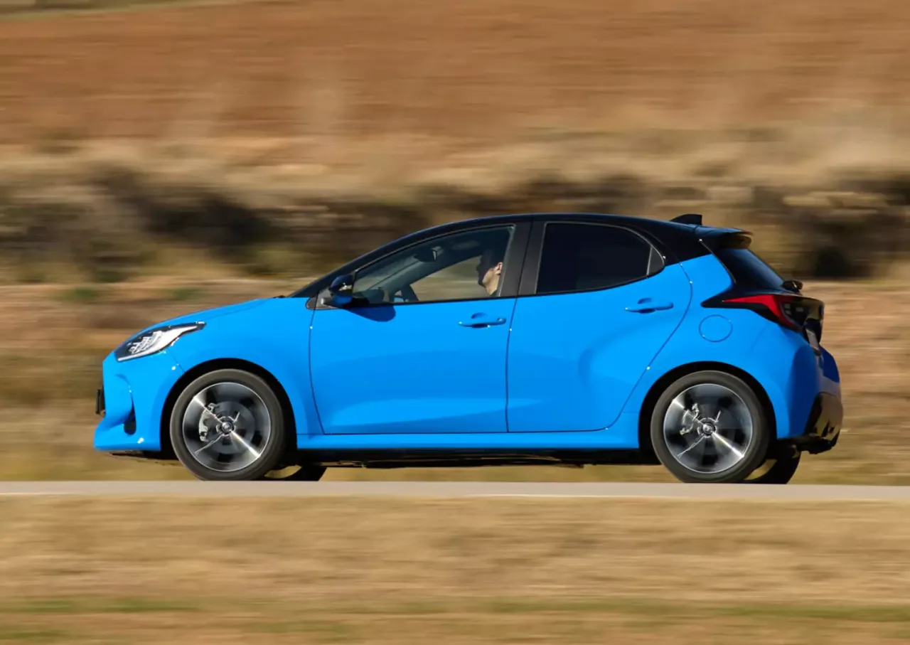 Błękitny samoch&oacute;d z czarnym dachem, idealne pierwsze auto dla dziewczyny, pędzi po drodze.