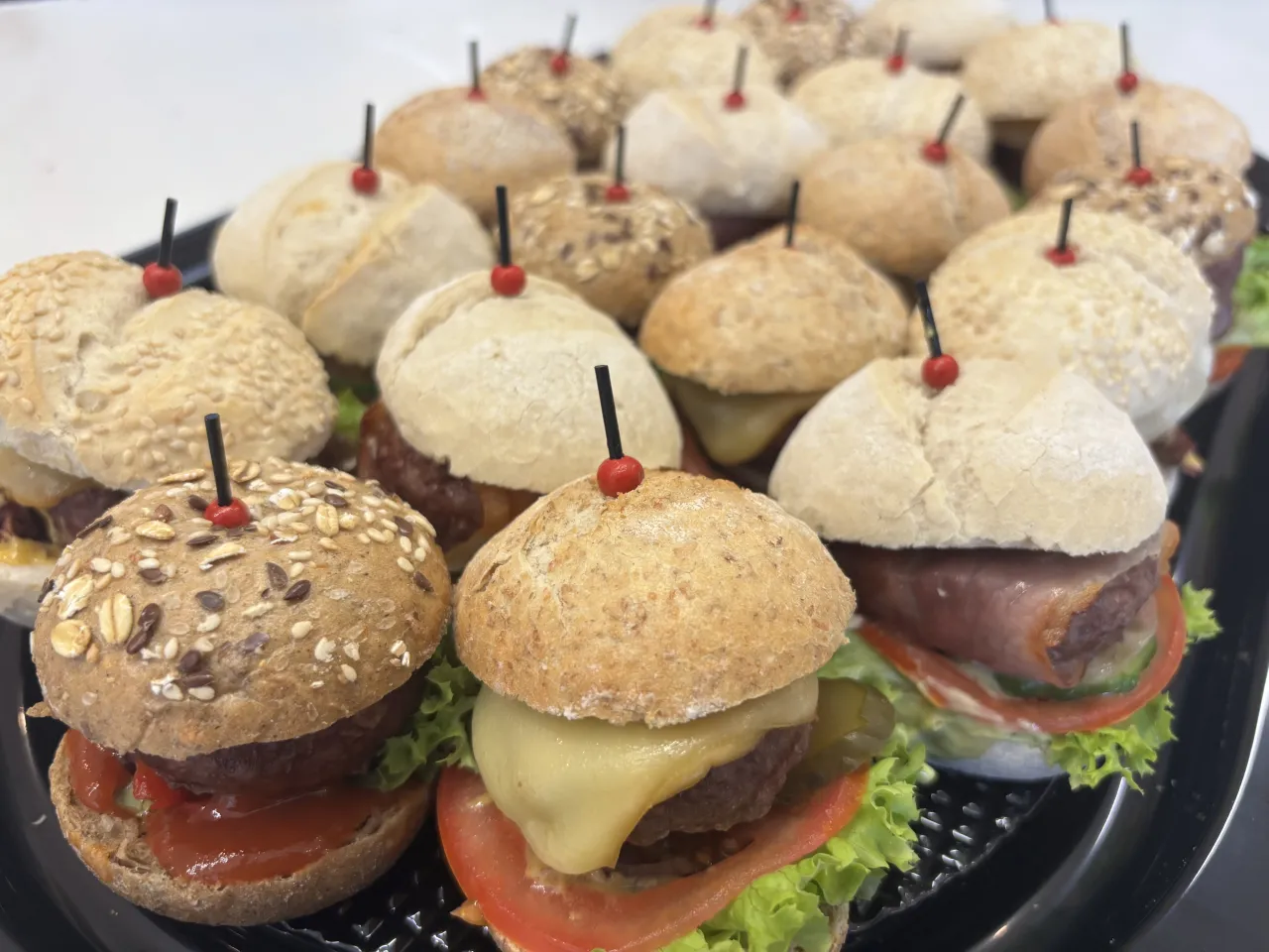 Mini hamburgery gdzie kupić? Taca pełna pysznych, małych burger&oacute;w z serem, warzywami i r&oacute;żnymi bułkami. Idealne na imprezę!