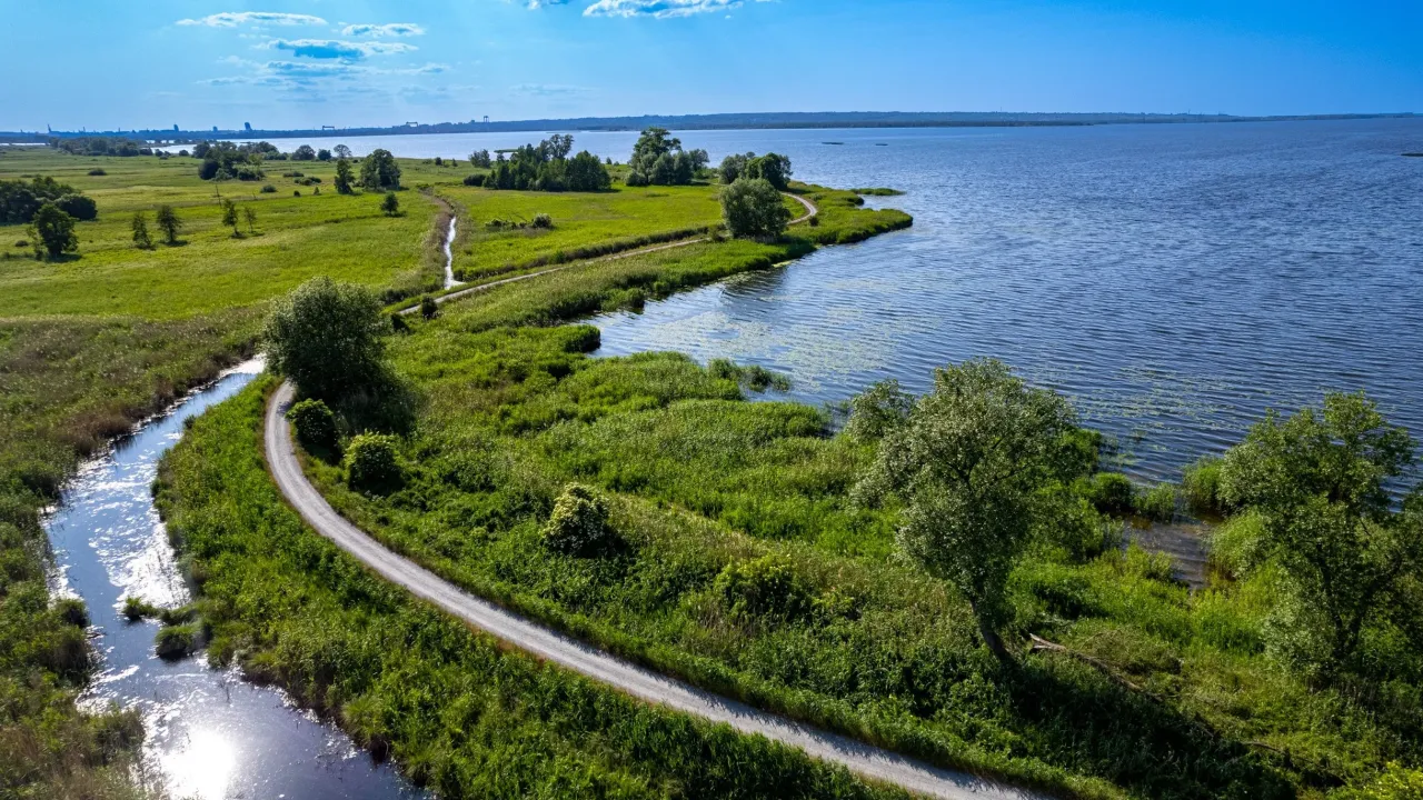 Malownicza ścieżka rowerowa wije się wśród zieleni, prowadząc wzdłuż spokojnego jeziora. Idealne miejsce na relaksujące trasy rowerowe wokół jeziora.