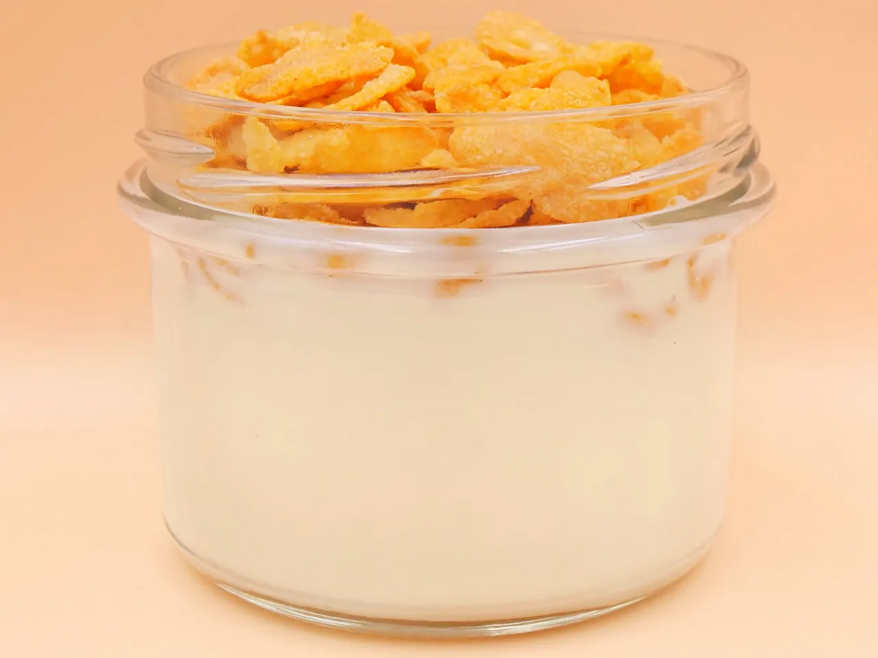 Szklany słoiczek z mlekiem i płatkami kukurydzianymi na wierzchu. Zastanawiasz się, ile kalorii ma miska płatków z mlekiem?