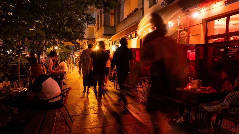 Anwohner blickt genervt aus dem Fenster auf eine laute Restaurantterrasse bei Nacht