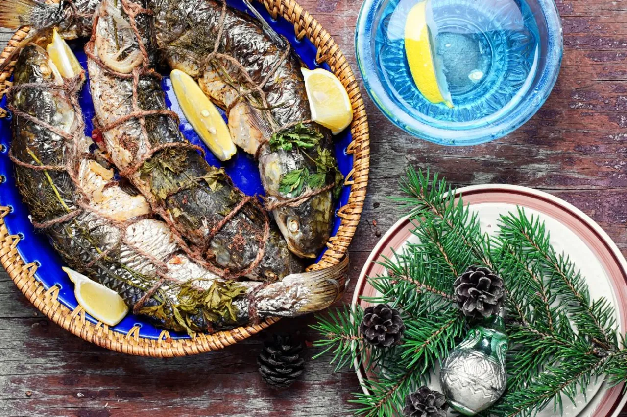 Ryba pieczona w folii, podana z cytryną, obok napoju i świątecznej dekoracji.