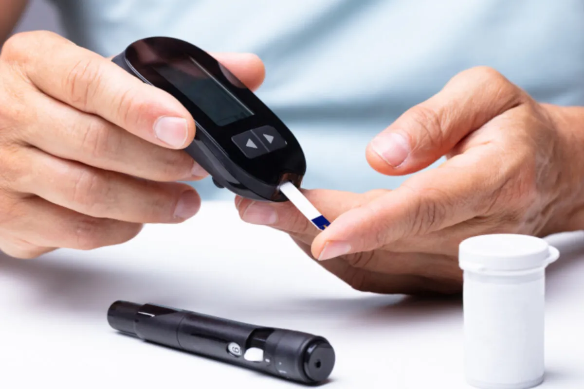 Osoba mierzy poziom cukru we krwi. Czy paski do glukometru są darmowe dla seniorów? Obok leży nakłuwacz i pojemnik na paski.