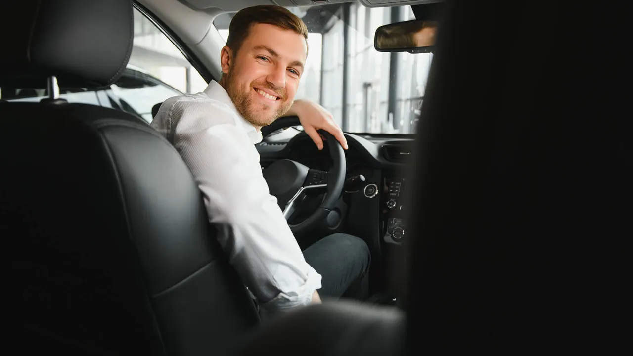 Uśmiechnięty mężczyzna za kierownicą, gotowy do pracy. Dowiedz się, jak zostać kierowcą Opti Taxi i zacznij zarabiać!