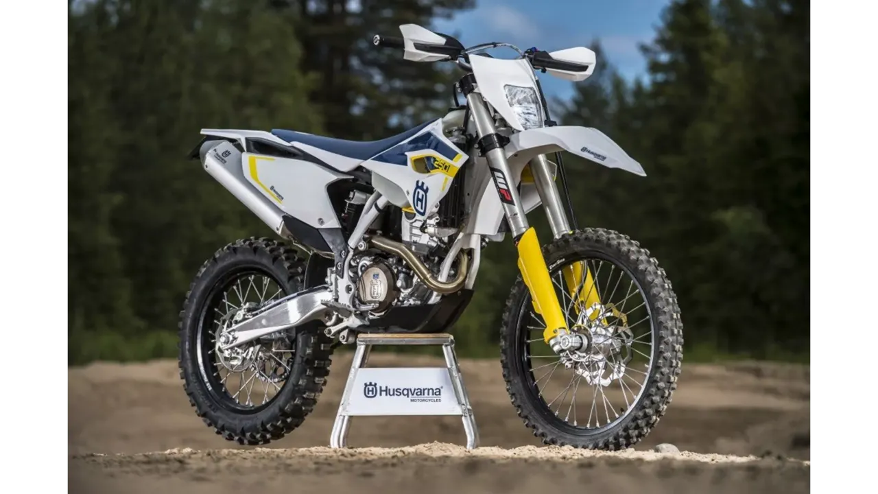 Potężny motocykl Husqvarna 250 FE gotowy na terenowe wyzwania. Biało-niebieska maszyna z żółtymi akcentami prezentuje się imponująco.
