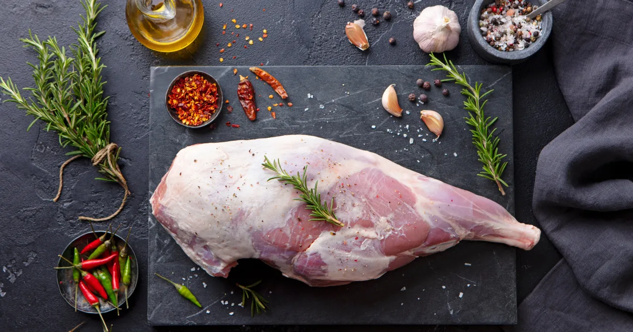 Surowa jagnięcina, gotowa do pieczenia. Obok gałązka rozmarynu, czosnek, chili i oliwa. Co to za pyszne danie?