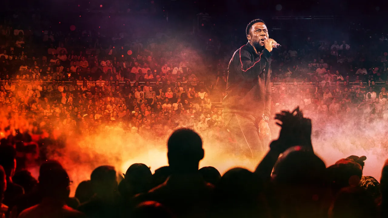 Kevin Hart stand up na scenie, rozbawiający tłum widz&oacute;w w ogniu świateł i dymu.