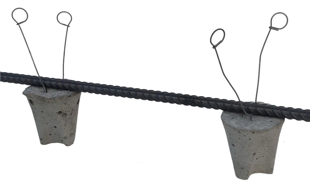 Dwa stożkowe dystanse do zbrojenia podtrzymują stalowy pręt, zapewniając mu odpowiednią odległość od powierzchni.