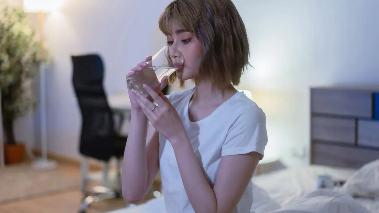 osoba pijąca wodę z butelki w nocy