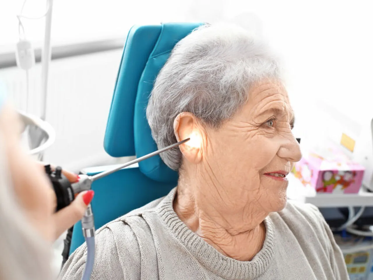 Starsza pani uśmiecha się podczas badania słuchu. Lekarz bada jej ucho otoskopem.