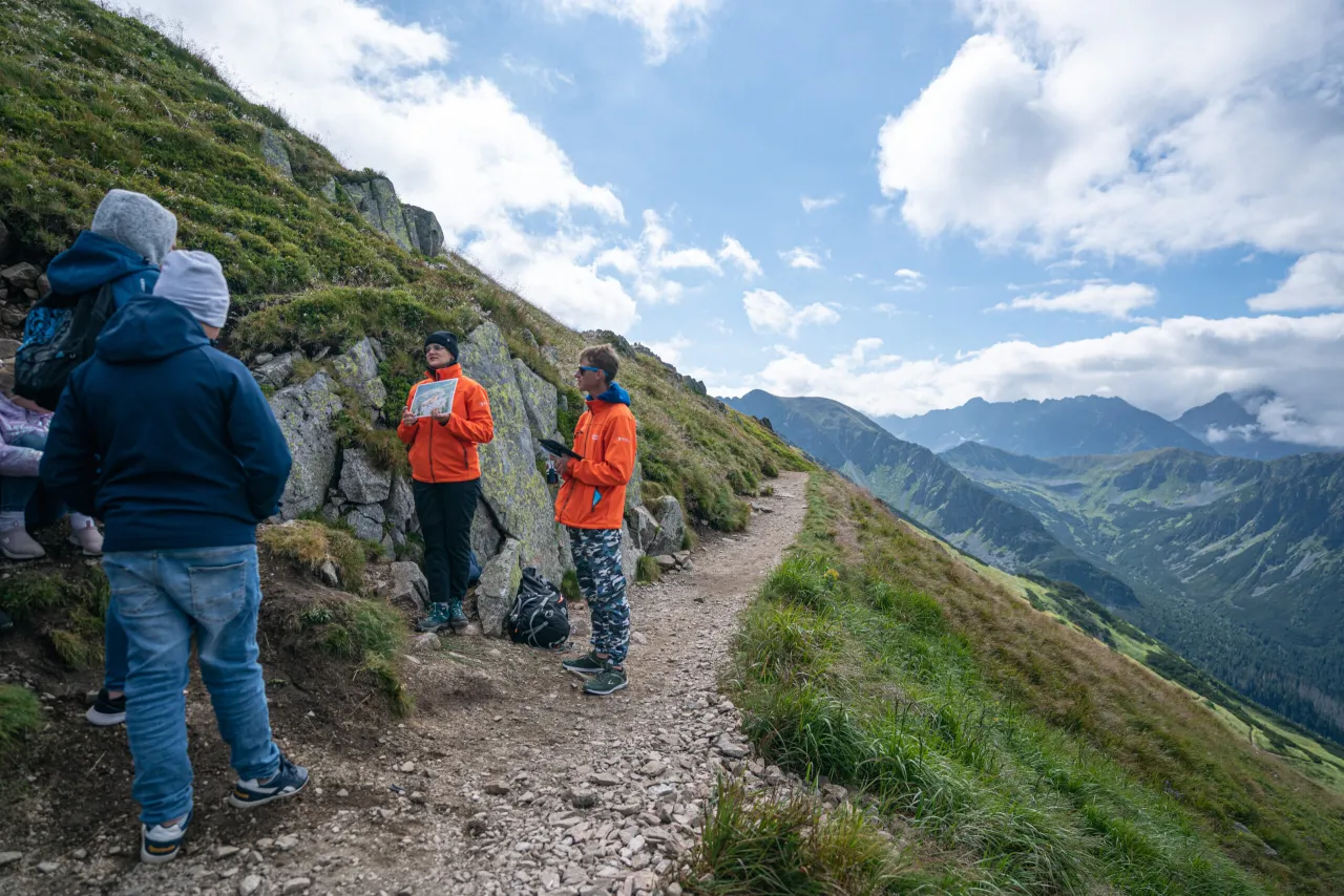 Grupa turystów na szlaku w Tatrach, podziwiających widok. Zastanawiają się, ile km jest na Kasprowy Wierch.