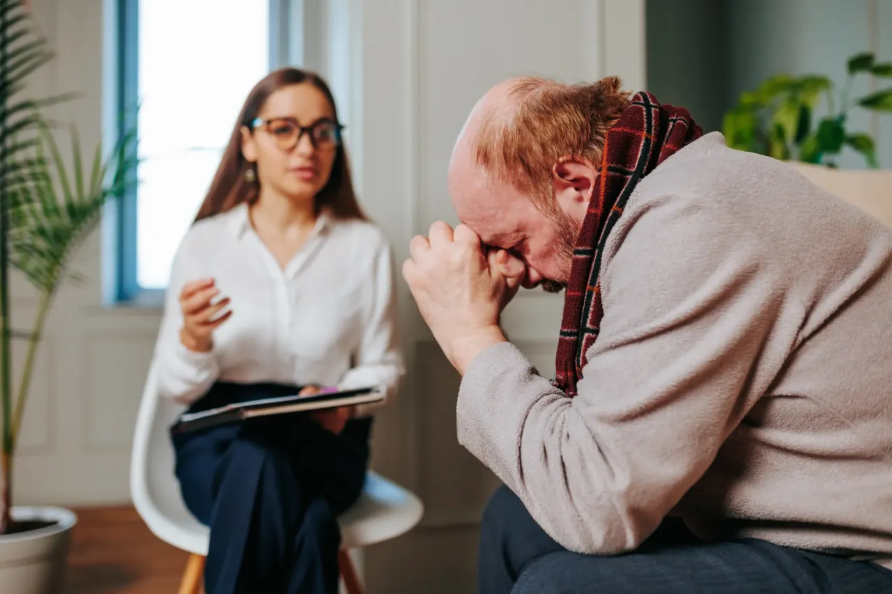 Dojrzała kobieta w okularach, z książkami medycznymi, uśmiechnięta, w tle uniwersytet