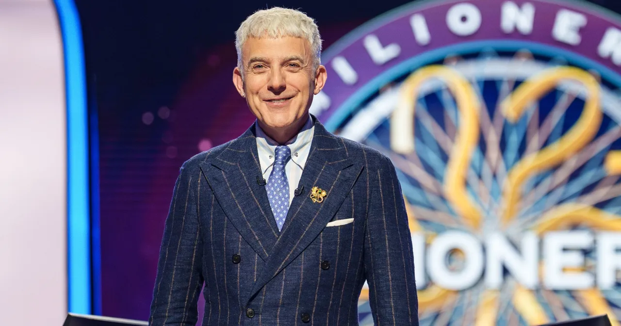 Uśmiechnięty Hubert Urbański w garniturze, gotowy do rozpoczęcia programu Milionerzy.